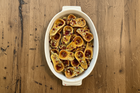 Roasted Honeynut halves in a white baking dish with pomegranate seeds and chopped nuts