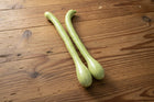 Two pale green Tromboncino squash with long slim necks and bulbed ends on a wooden tabletop