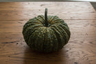 Thai Kang Kob pumpkin, a whole dark green warted and deeply ribbed fruit on a wooden table